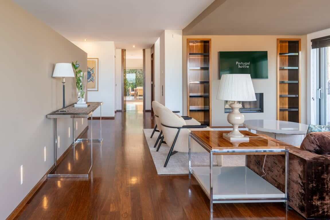 A modern hotel room with a wooden floor, a sofa, a coffee table, a lamp, and a bookshelf.