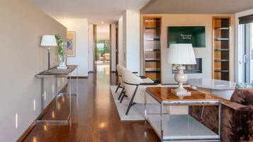 A modern hotel room with a wooden floor, a sofa, a coffee table, a lamp, and a bookshelf.