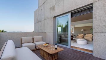 A modern outdoor seating area with a wooden table, cushioned sofas, and a glass door leading to an interior space with a round table and chairs.
