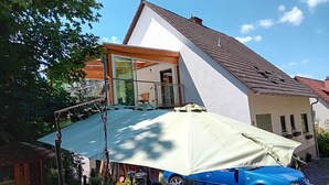 A house with a balcony, a blue car parked in front, and a dog near the car. - Vacation cottage Wasgaublick (Bundenthal, Rheinland-Pfalz, Deutschland)