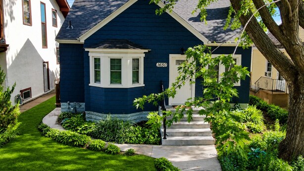 Una casa residencial con fachada azul oscuro, un ventanal saliente, una puerta principal y el número 1650 en la pared.