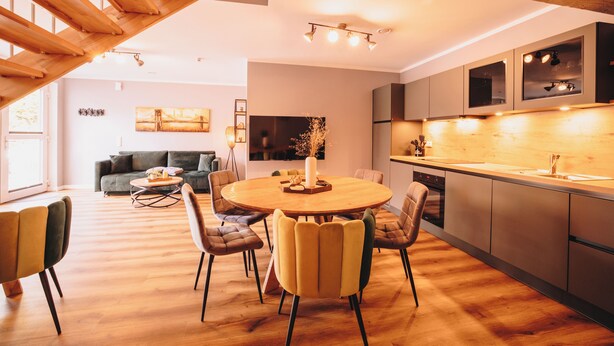 Cozinha moderna com ilha central, sala de jantar com mesa redonda e sala de estar com sofá e mesinha de centro.