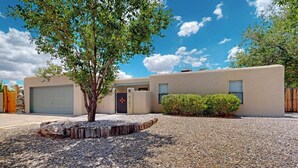 A modern house with a garage, a tree, and a gravel driveway. - Balloon Fiesta foothills Hidden Gem (Albuquerque)