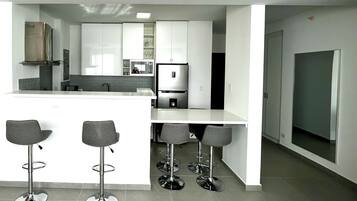 Una cocina moderna con armarios blancos, una campana extractora de acero inoxidable y un microondas integrado. Hay cuatro taburetes de bar y una isla grande con un fregadero.