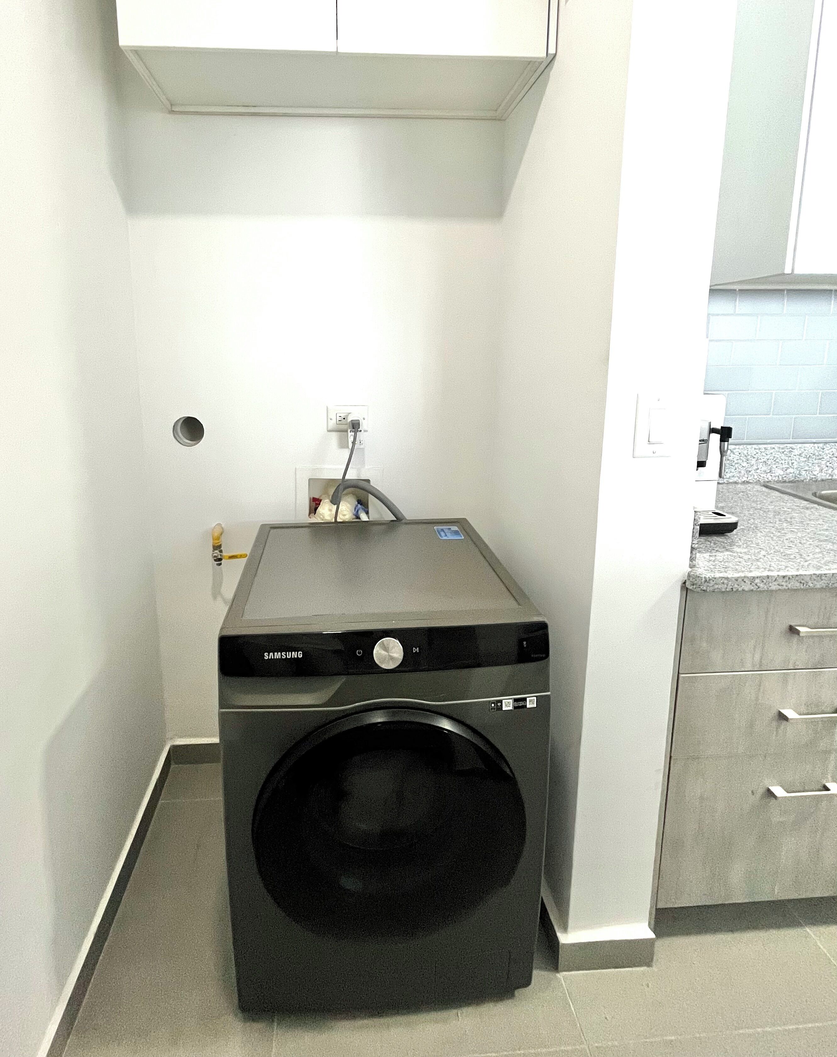 A compact, modern laundry room with a front-loading washing machine, a small sink, and a countertop with a faucet.