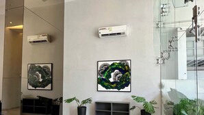A modern interior with a glass wall, two air conditioning units, and two grey ottomans.