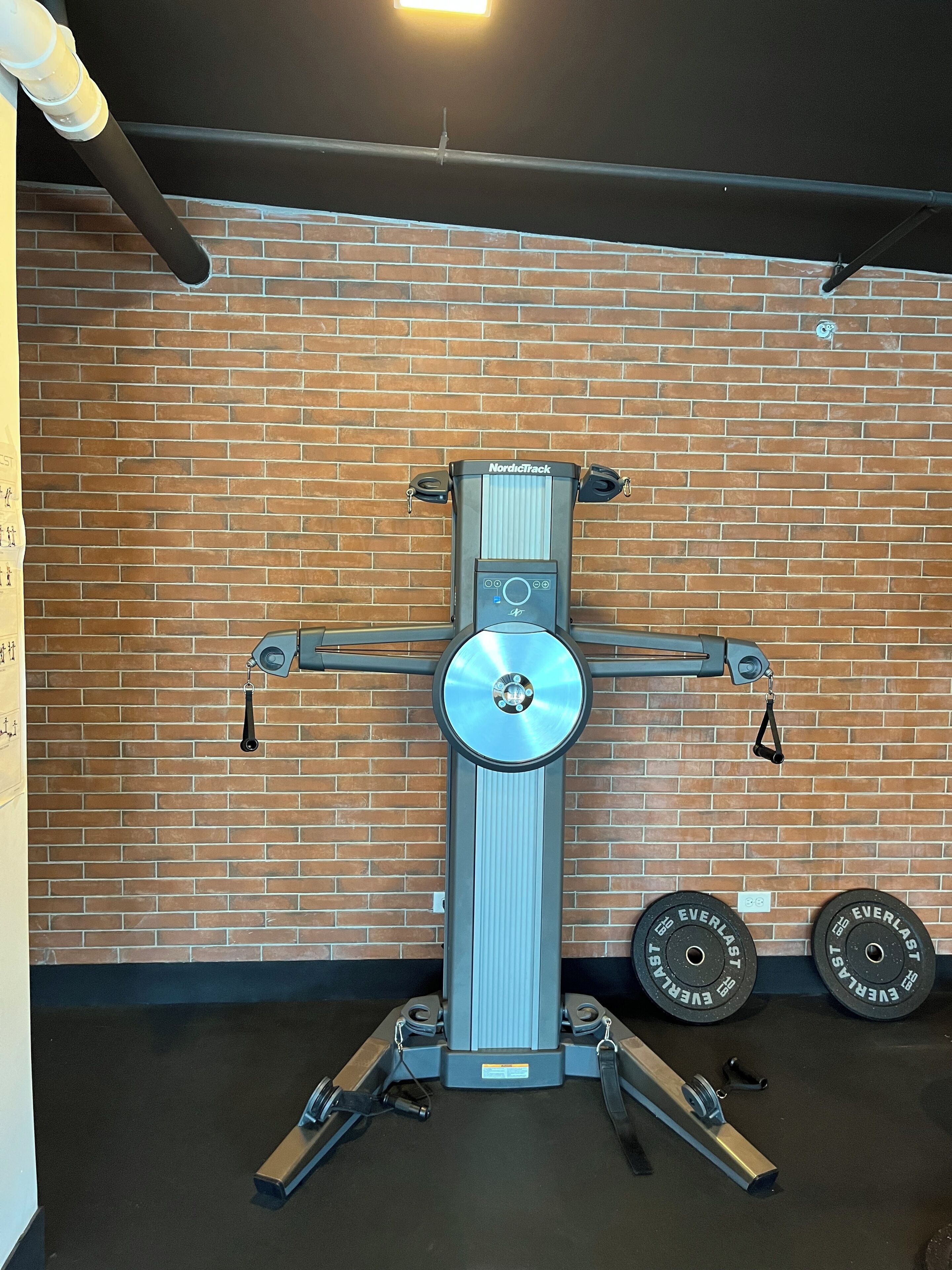 Uma máquina de exercícios NordicTrack encostada a uma parede de tijolos, com dois pesos no chão marcados com a inscrição "EVERLAST".