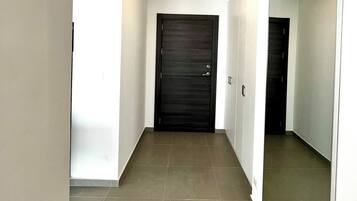 A hallway with a dark door, white walls, and tiled flooring.