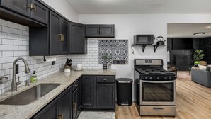 A modern kitchen with dark cabinets, a granite countertop, a stainless steel sink, a microwave, and a built-in oven. - Arlington Retreat Near Stadiums and Six Flags (Arlington)