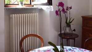 A dining area with a table covered in a floral tablecloth, a window with a view of buildings, and a radiator. - IL GINEPRO R&B (Monghidoro)