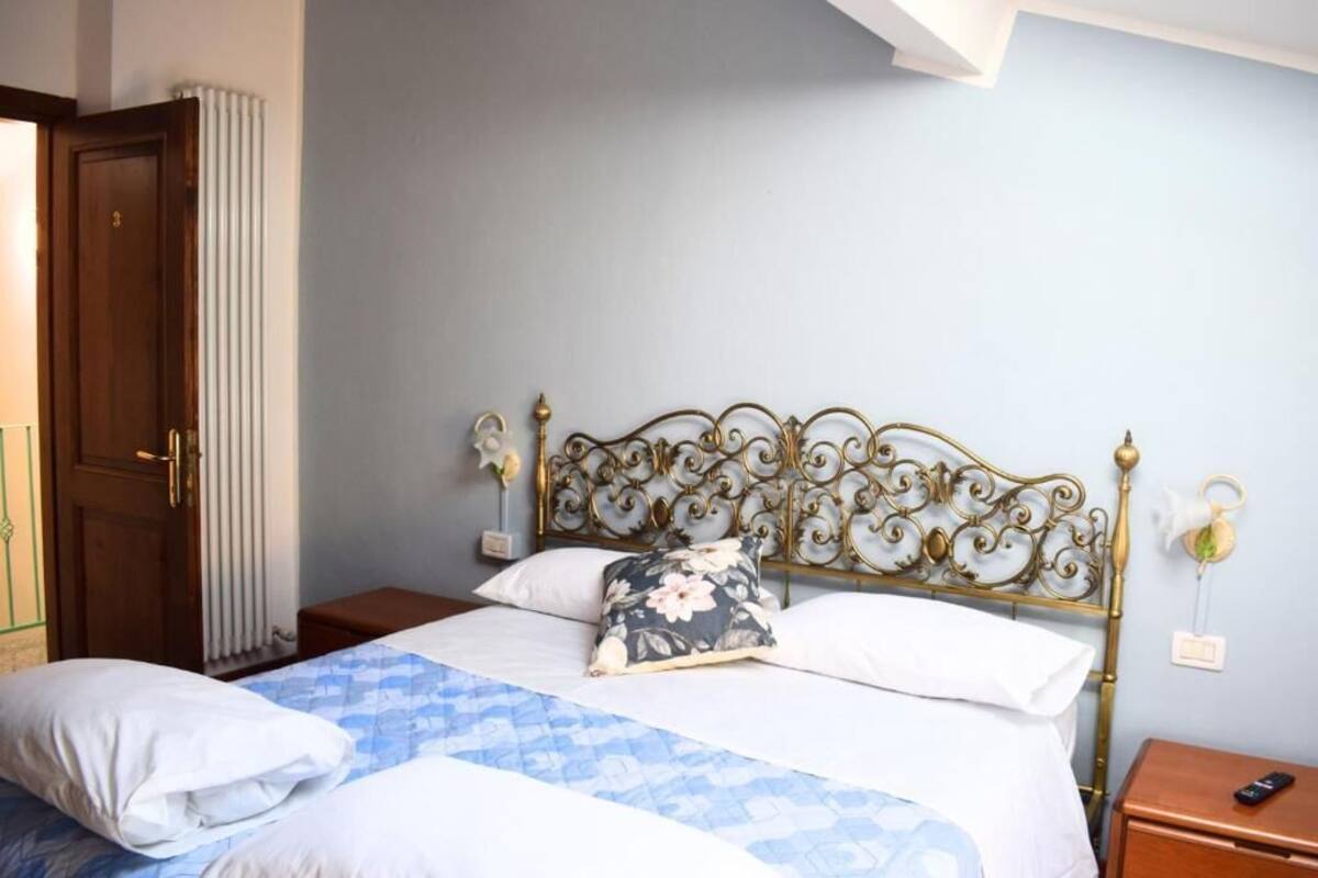 A bedroom with a bed, a wooden door, a radiator, and a nightstand with a remote control.