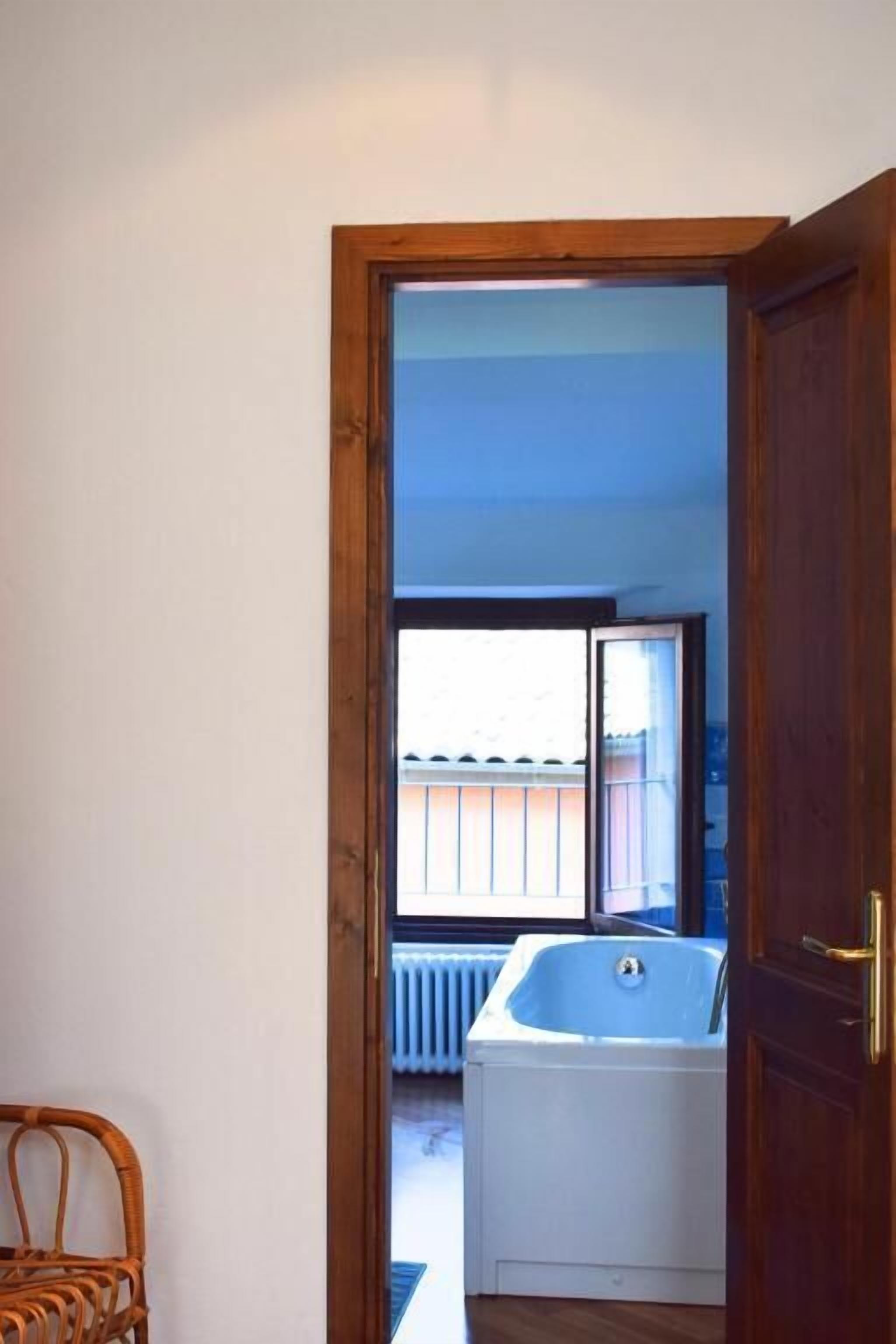 A doorway leading to a room with a bathtub, a wicker chair, and a view of a balcony.