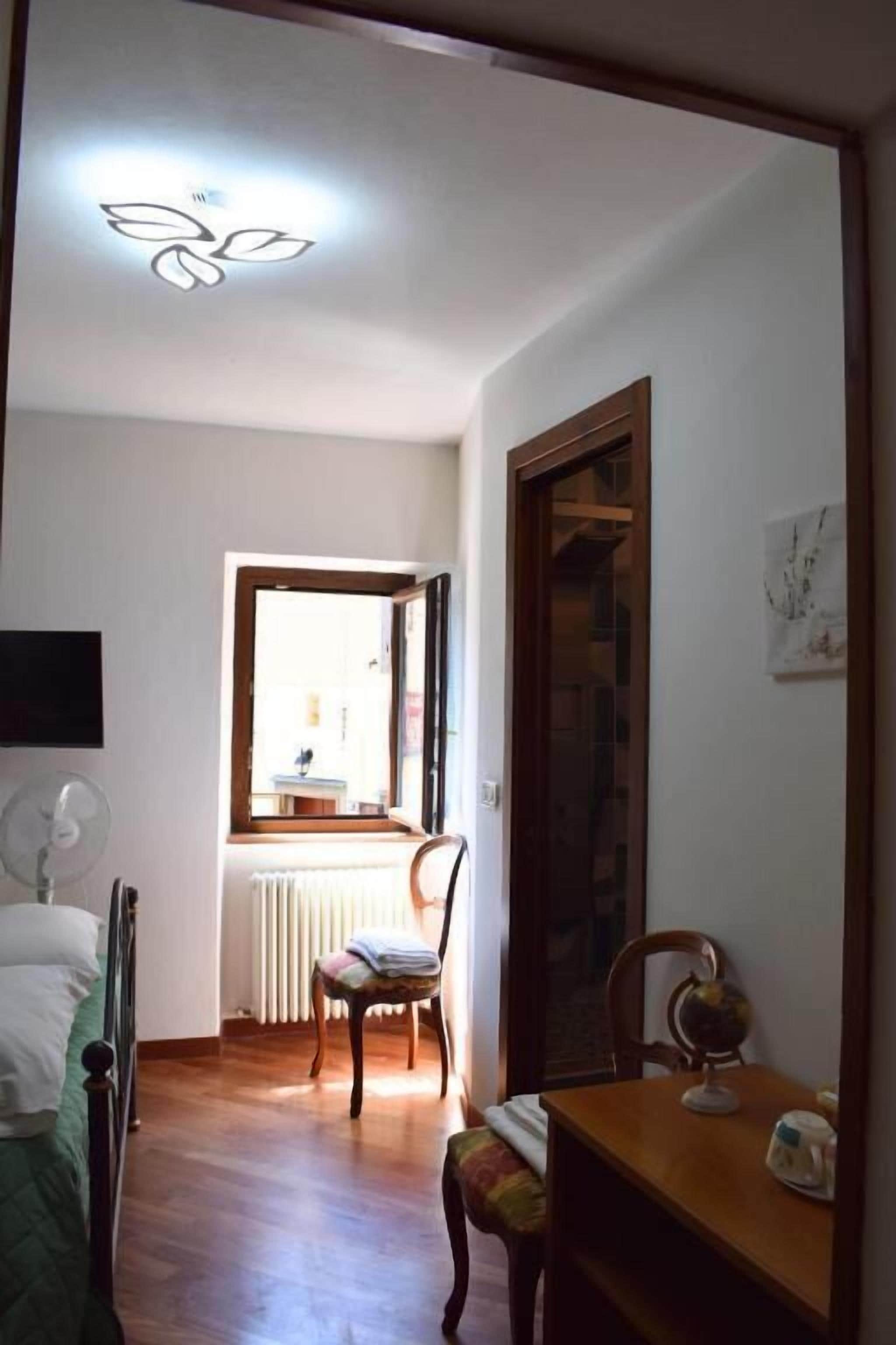 A room with a bed, a chair, a table with a globe, a window, and a radiator.
