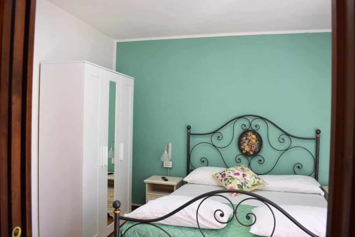 A bedroom with a bed, a nightstand, a wardrobe, and a wall with a decorative item.