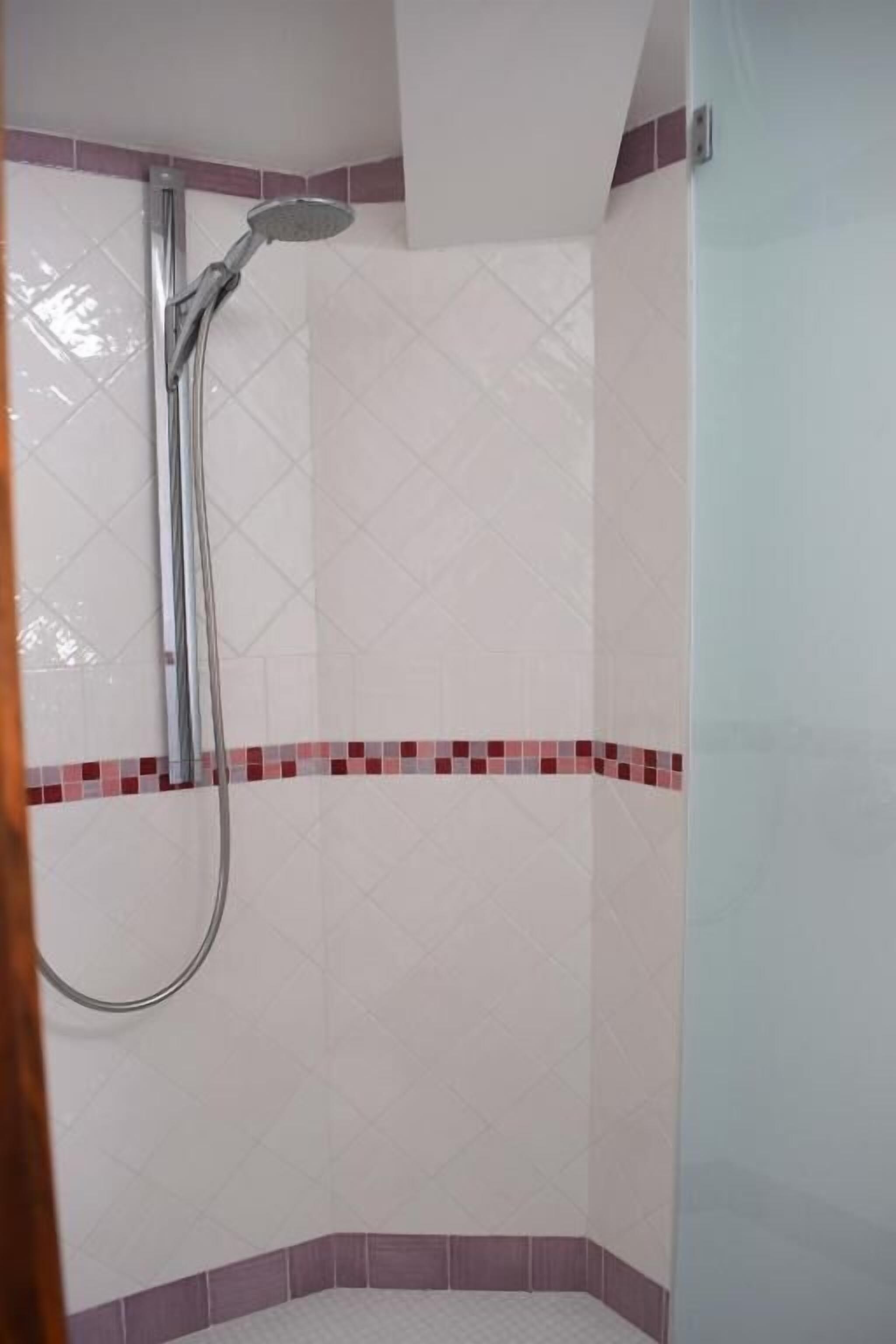 Ducha con cabezal de ducha de mano, paredes de azulejos y diseño en esquina.