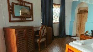 Una habitación con un escritorio de madera, una silla, una cama con colchón blanco, un espejo y una ventana con cortinas.