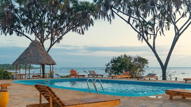 Zona de piscina con sillones de descanso, una estructura de techo de paja y vista al mar.