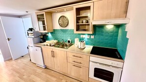 Cocina compacta con armarios de madera, un microondas, un fregadero, un tostador y un reloj en la pared.