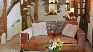 Una sala de estar acogedora con un sofá de cuero marrón, una escalera de madera y una pared de piedra.