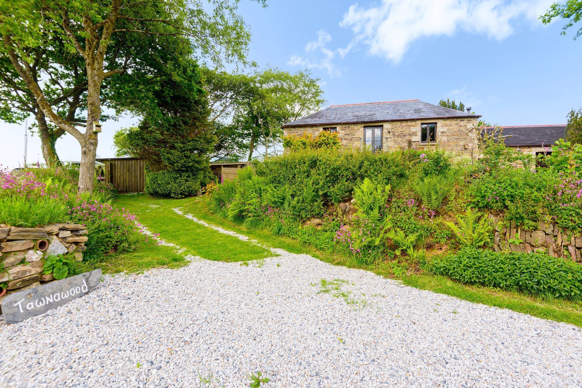 A stone house with a gravel driveway leading to a wooden gate.