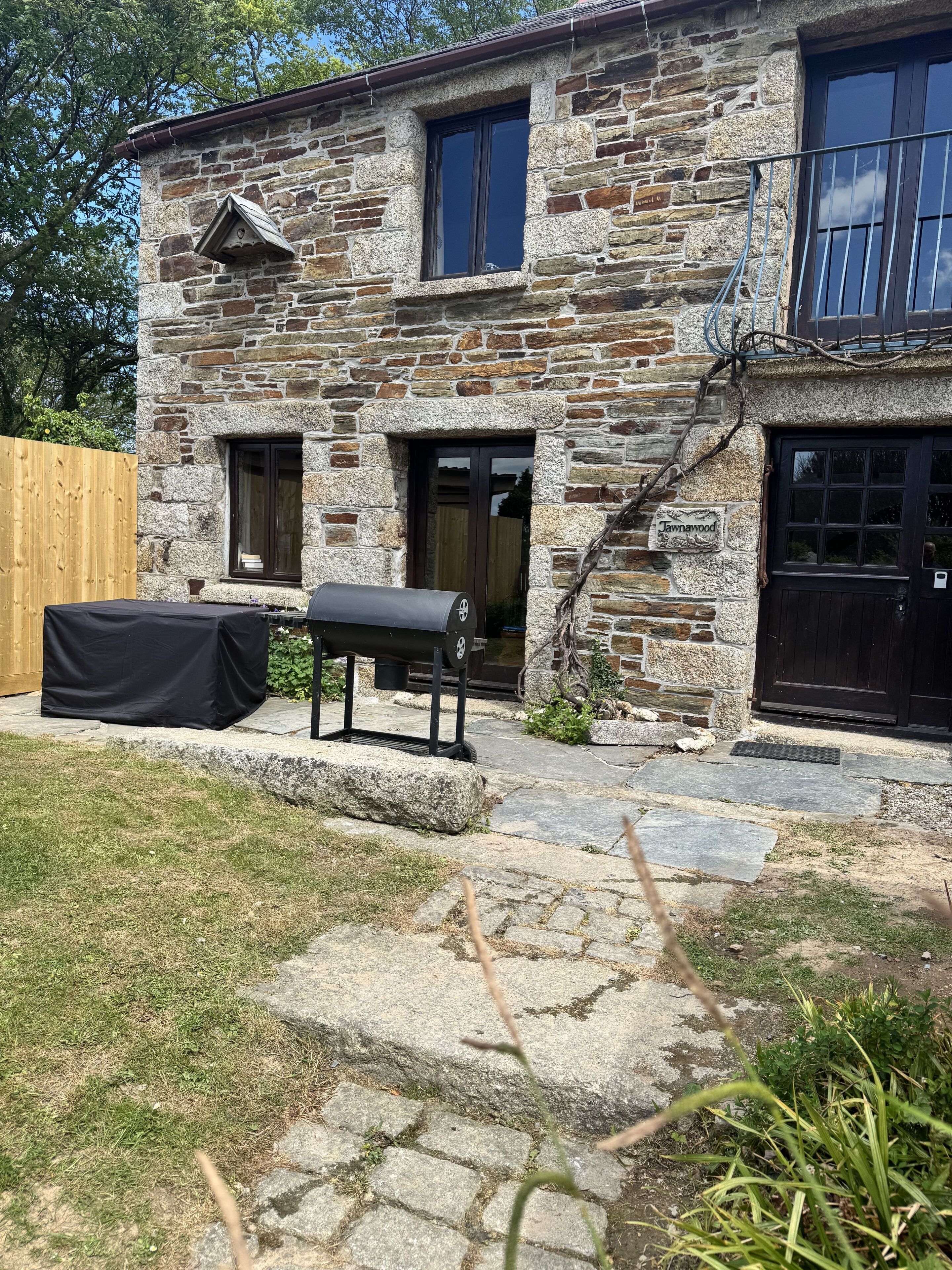 Una casa in pietra con un'area barbecue coperta, una recinzione in legno e un vialetto in pietra che conduce all'ingresso.