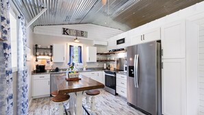 A modern kitchen with white cabinetry, a stainless steel refrigerator, and a wooden island with stools. - Charming 2-bedroom barn in, Foley 8 miles to Beach, dogs welcome, near Sportplex (Foley)