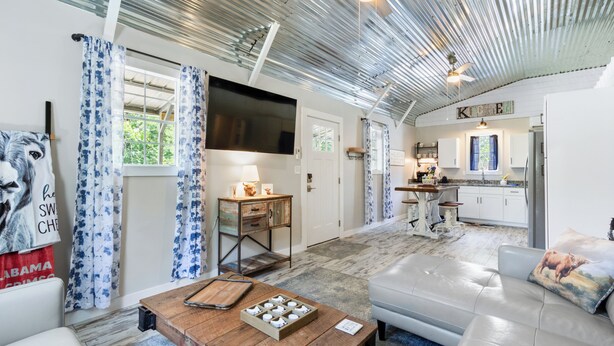 A spacious living area with a large sofa, a wooden coffee table, and a flat-screen TV mounted on the wall. - Charming 2-bedroom barn in, Foley 8 miles to Beach, dogs welcome, near Sportplex (Foley)