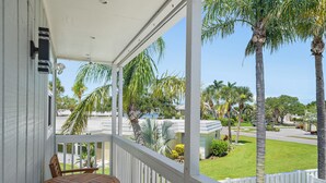 A covered porch with a wooden table and chairs, overlooking a well-maintained lawn and palm trees. - Fresh Coastal Comfort, Beaches Close & Bay Views, 2 GB WIFI (Sarasota)