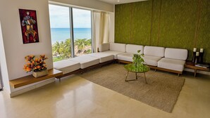 A modern living room with a large window, a green textured wall, a white sofa, a glass coffee table, and a painting.