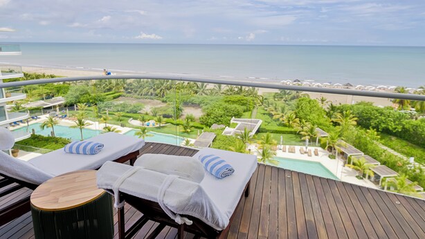 A balcony with two sun loungers, a pool, and a view of the beach and ocean.