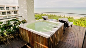 A wooden deck with a hot tub and lounge chairs overlooking a beach.