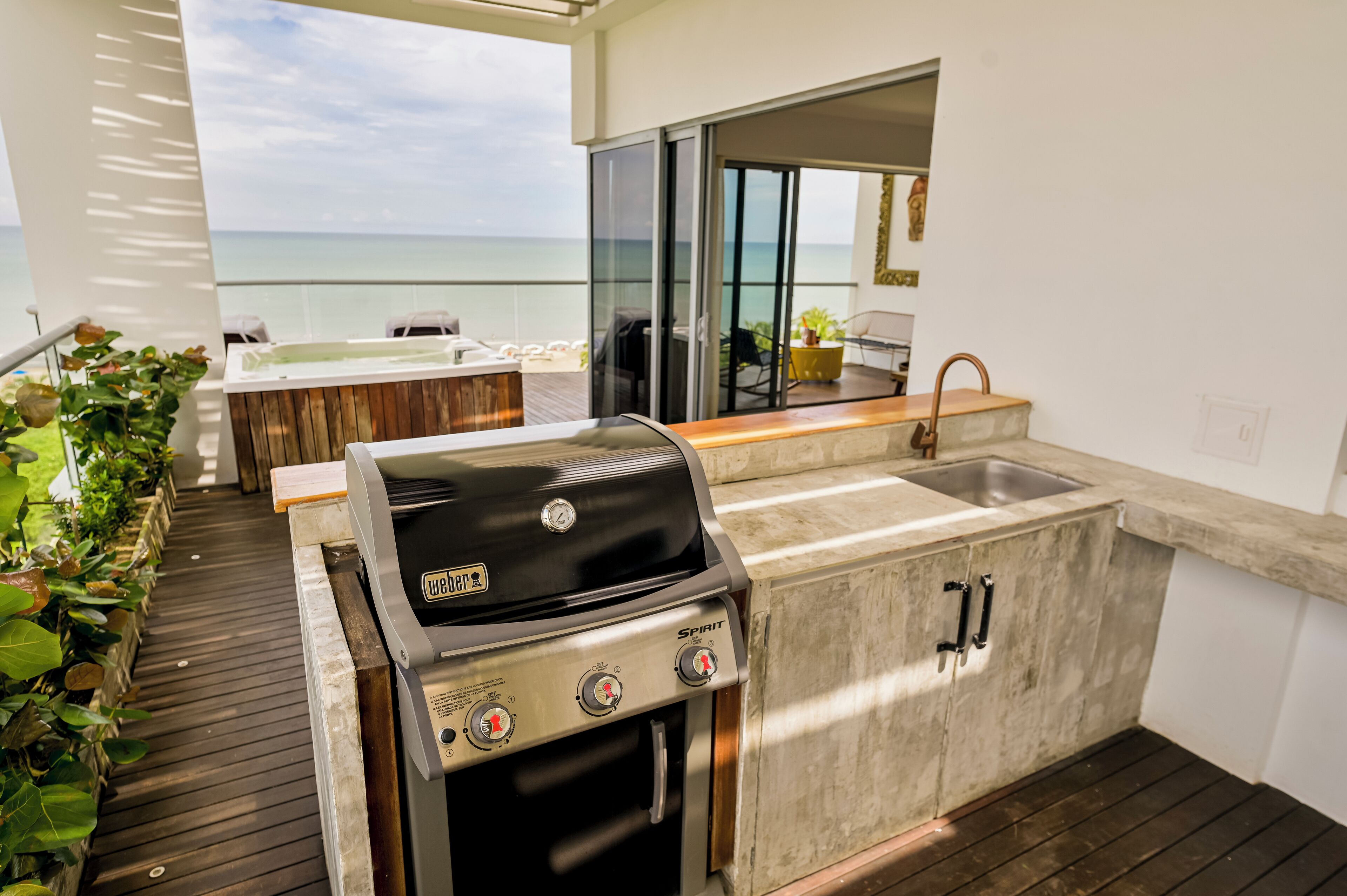 Cocina exterior con parrilla, pileta y terraza de madera con vista al océano.