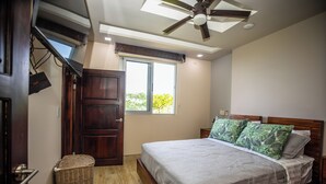 A bedroom with a bed, a ceiling fan, a window, and a door.