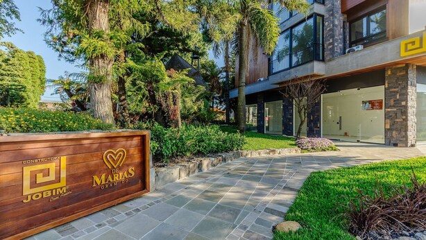 A modern building with a wooden signboard, a paved pathway, and lush greenery. - Beautiful Apartments in Gramado - DMS (Gramado)