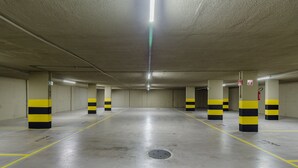 A parking garage with concrete pillars, yellow and black stripes, and a manhole cover. - Beautiful Apartments in Gramado - DMS (Gramado)