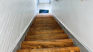 A wooden staircase with white walls and a metal handrail, leading to a door at the top.