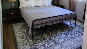 Un dormitorio con cama, dos mesitas de noche, ventilador de techo y ventana con cortinas.