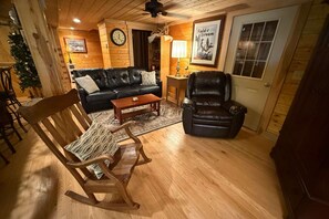 Ein gemütliches Wohnzimmer mit Holzboden, einer schwarzen Ledersofa, einem Holzschaukelstuhl, einem Couchtisch und einem Kamin.