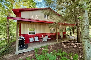 A cabin with a red and white exterior, a porch with chairs, and a grill outside.