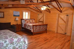 A wooden cabin bedroom with a bed, nightstand, lamp, and a ceiling fan.