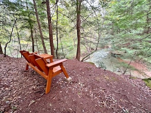 A wooden bench in a forested area with a view of a stream.