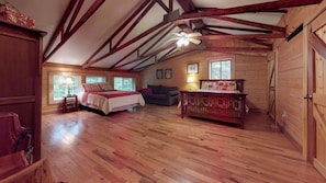 A spacious attic bedroom with wooden beams, a large bed, a sofa, and a wooden dresser.