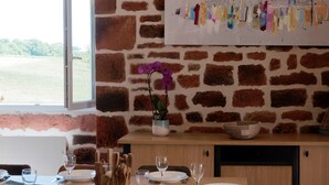 Ein Essbereich mit Steinwand, einem Fenster mit Blick auf Grünflächen, einem Tisch mit Tellern und Gläsern sowie einer Vase mit einem purpurfarbenen Orchideenblüten.