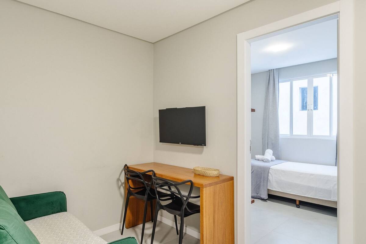 Ein kleiner, sauberer Raum mit einem Bett, einem Schreibtisch mit zwei Stühlen, einem Fernseher und einem Fenster mit Vorhängen.