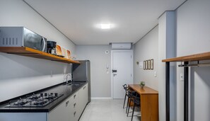 Une cuisine étroite, équipée d’une cuisinière à gaz, d’une machine à café et d’un four à micro-ondes placés sur une étagère. On y trouve également une table à manger avec des chaises et une petite plante.