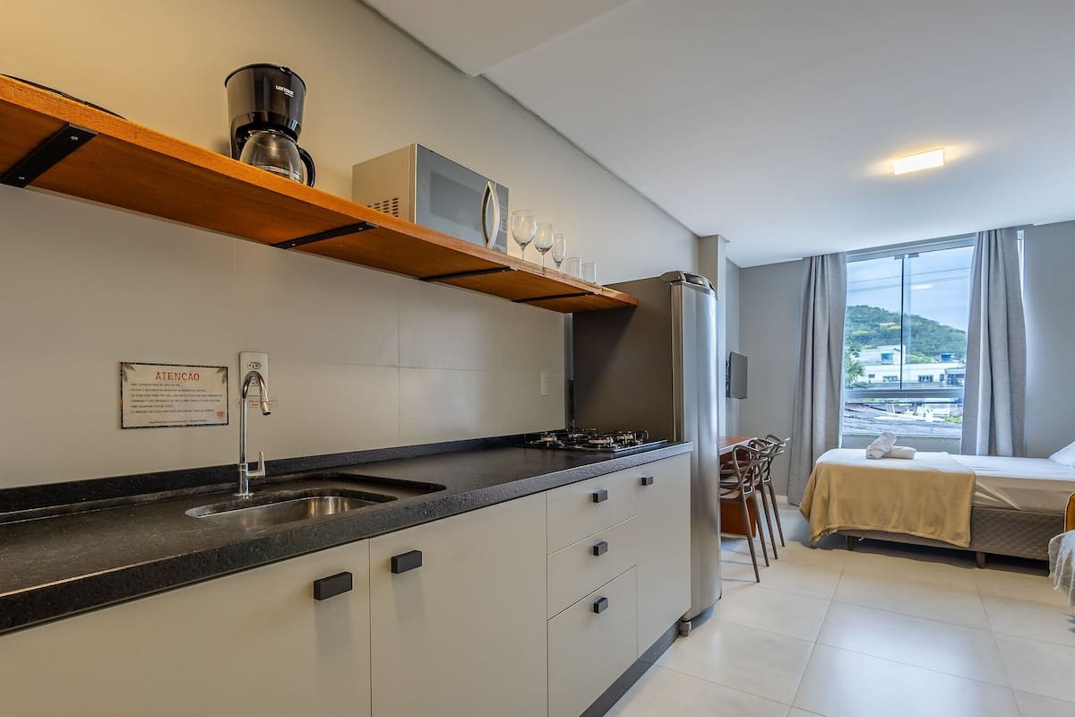 Eine moderne Küche mit Einbauherd, Kaffeemaschine und Spüle. Es gibt eine Essecke mit Tisch und Stühlen, und ein Bett mit Blick nach draußen.