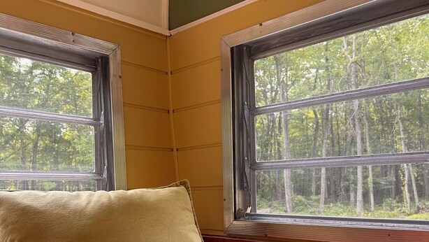 Una habitación con dos ventanas, un cojín beige y un cojín rojo sobre un sofá estampado.
