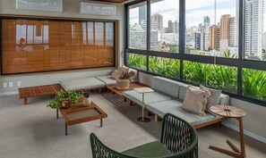 A modern living room with a large window, a sofa set, a coffee table, and a chair. - BLB - Apartments in Barra, Salvador (Salvador)