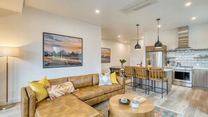 A modern living room with a leather sofa, a round coffee table, and a dining area with bar stools.