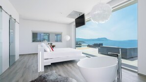 A modern bedroom with a large bathtub, a bed, and a view of the sea.